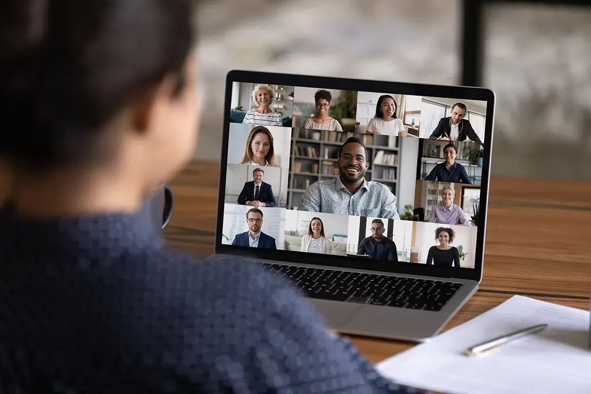 Person participating in a virtual meeting with a grid of colleagues on the laptop screen