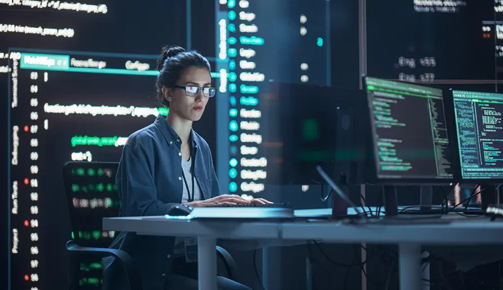 Woman coding and analyzing data on multiple computer screens in a high-tech environment