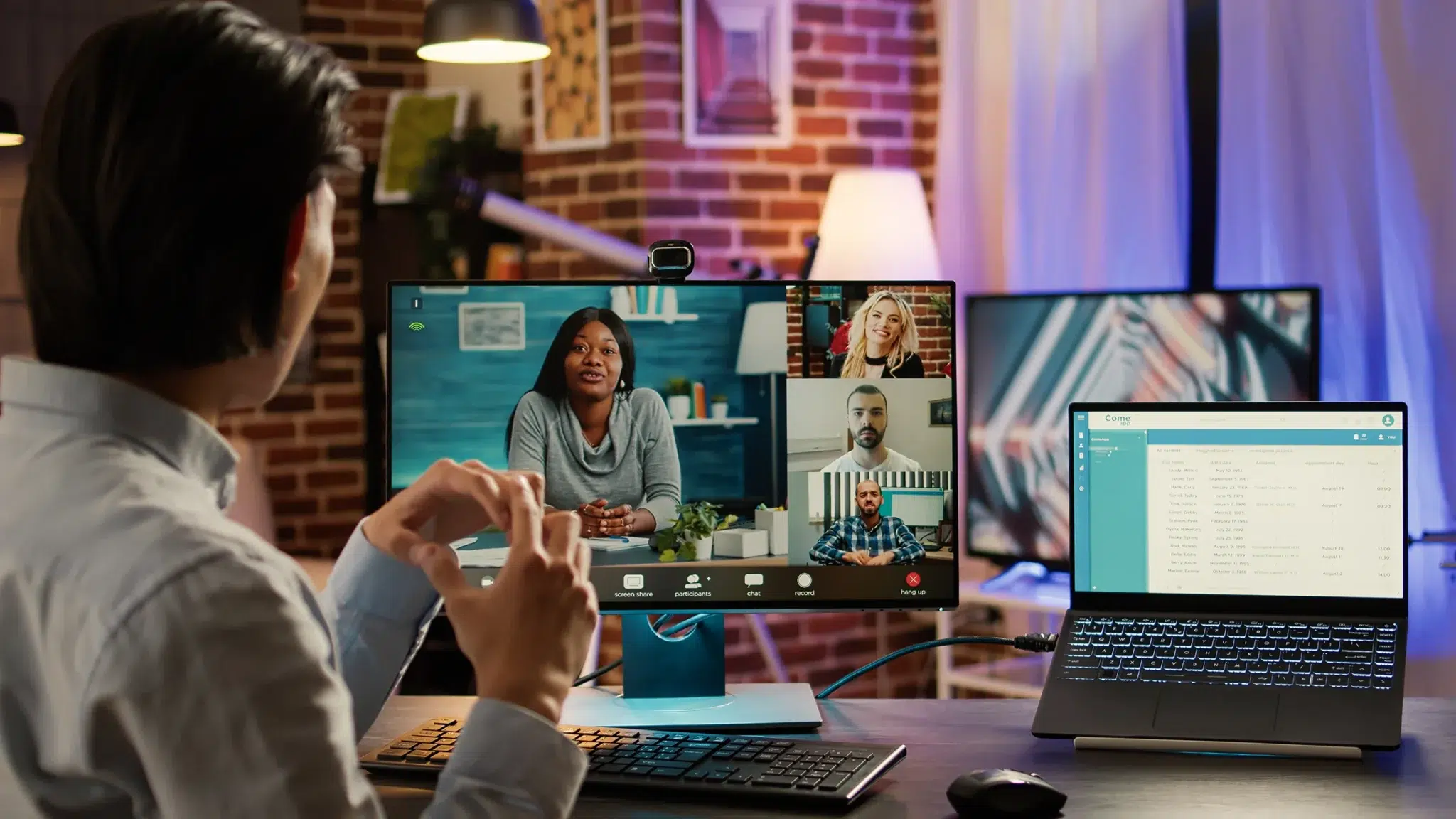 Person participating in a video conference with colleagues displayed on the screen while using a laptop in a modern workspace