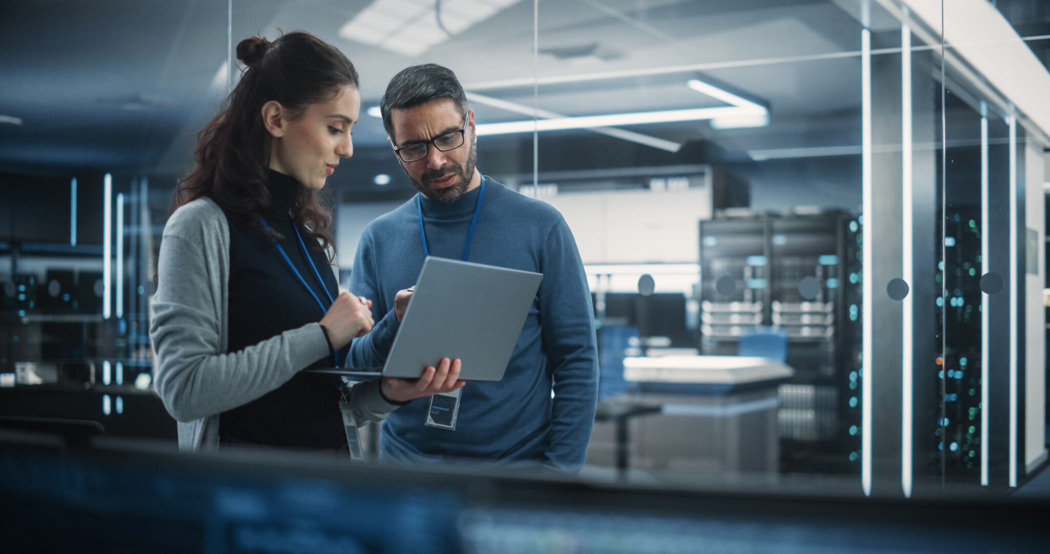 Two IT professionals discussing data on a laptop in a modern server room