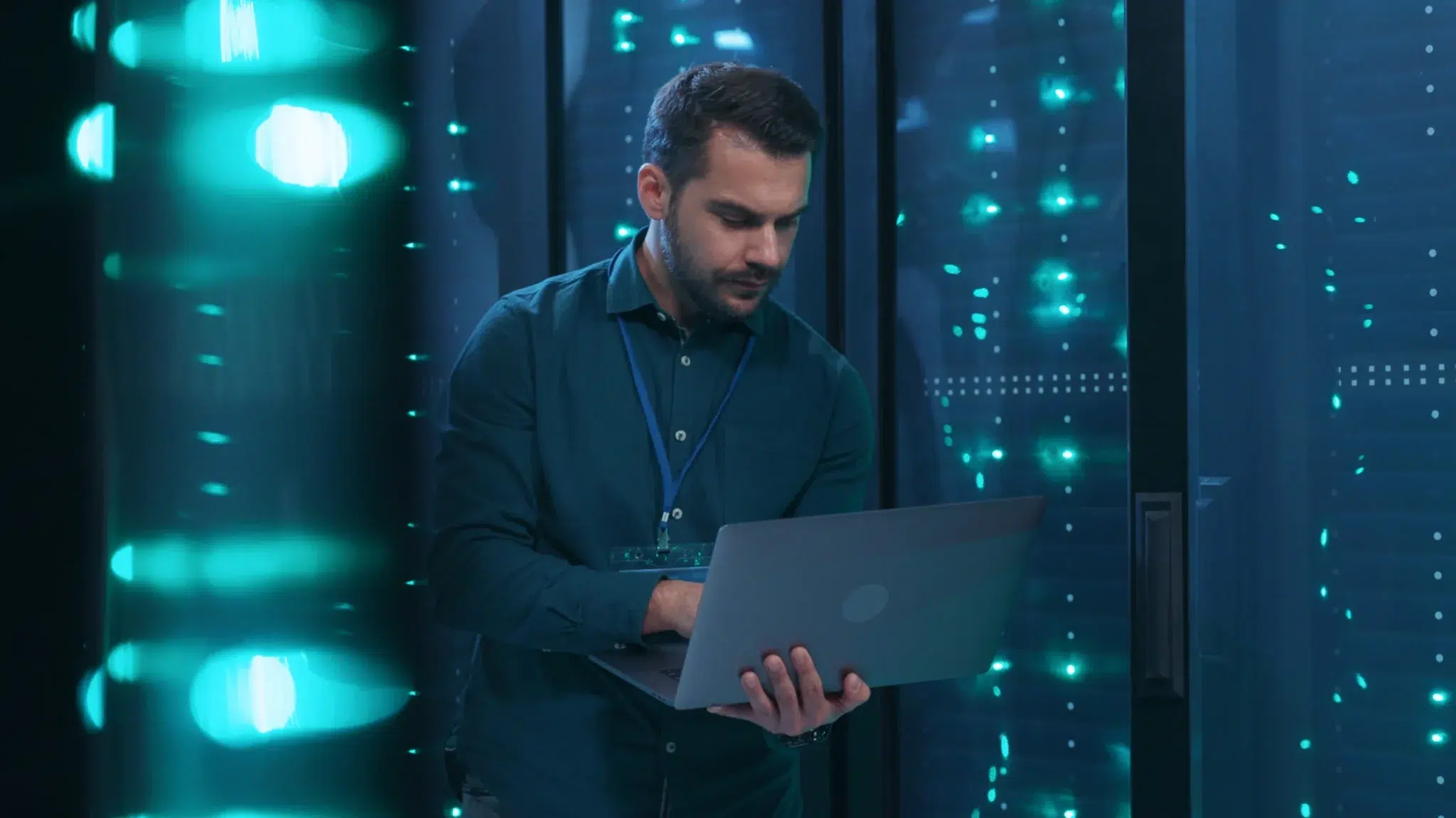 IT specialist inspecting a laptop while working in a server room with glowing blue lights.