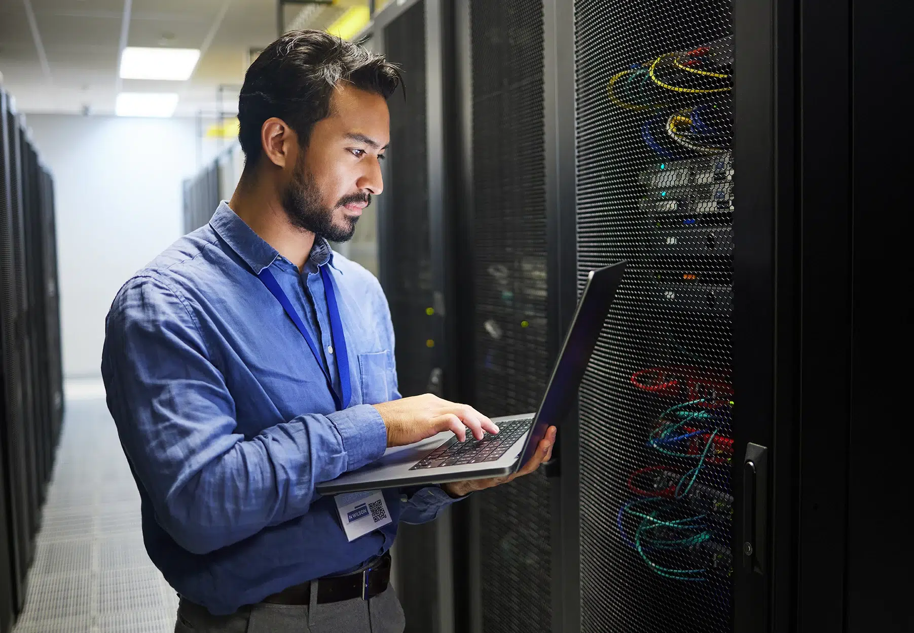 Network engineer using a laptop to troubleshoot server connections in a data center.